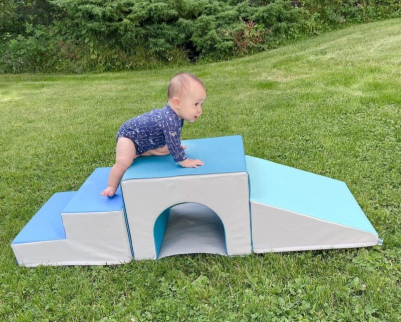 an infant crawling across a soft-play bridge outside