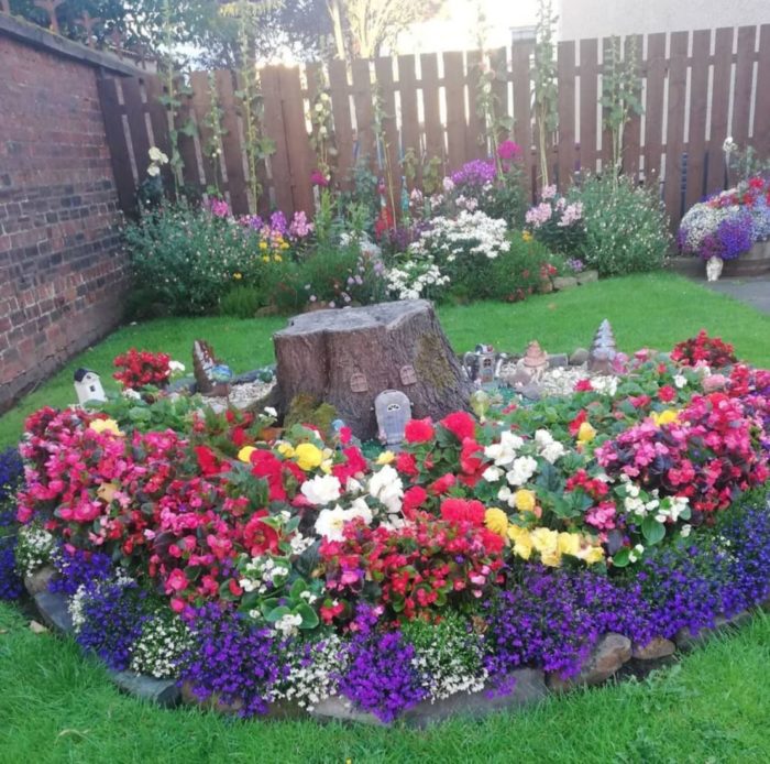 a flower bed with brightly coloured flowers and miniature fairy houses