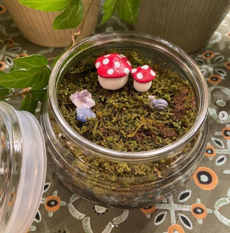 tiny toadstool sculptures on a layer of moss in a jam jar fairy garden