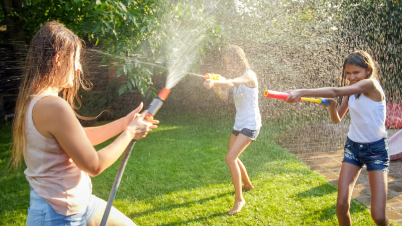 three tweenage children spraying water hoses at each other in a garden