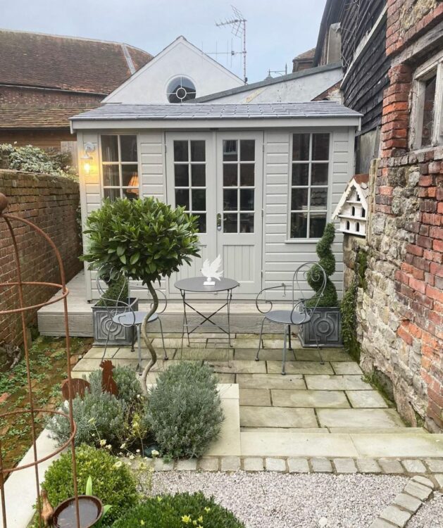 a sage green garden cabin at the back of a small garden