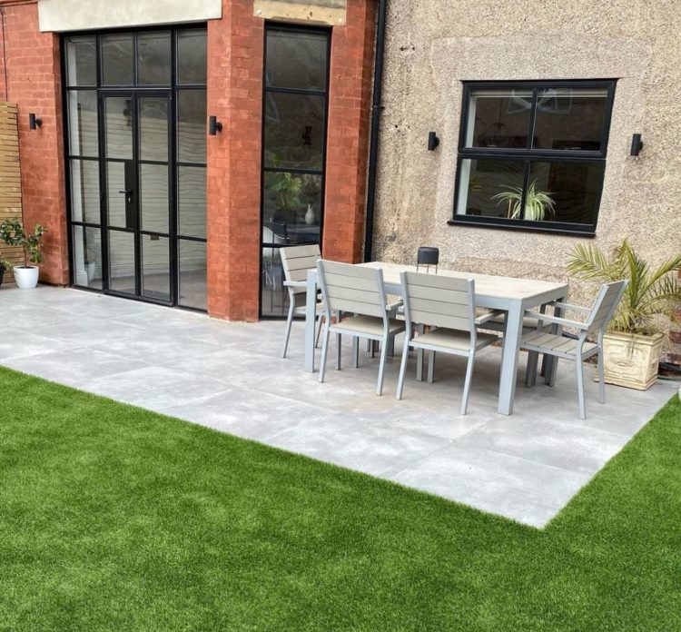 a clean grey patio surrounded by a perfectly manicured lawn, outside a red brick building with industrial style windows