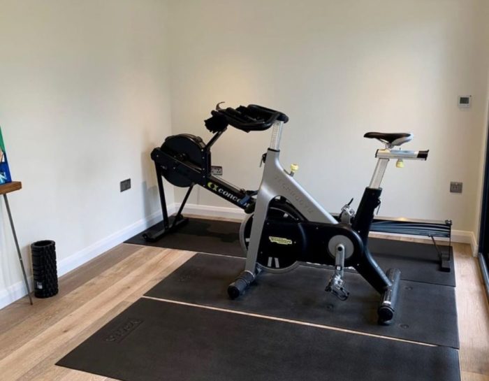 a simple garden cabin interior with exercise equipment on rubber mats to protect the wooden floor