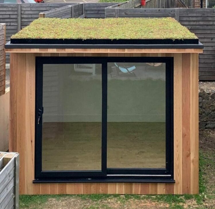 a small garden cabin with glass doors and a green roof