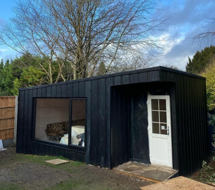 a matte black garden cabin with a large window to one side