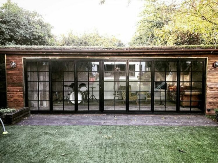 a large garden building made from bricks with big industrial-style windows - inside there's seating and a drum kit