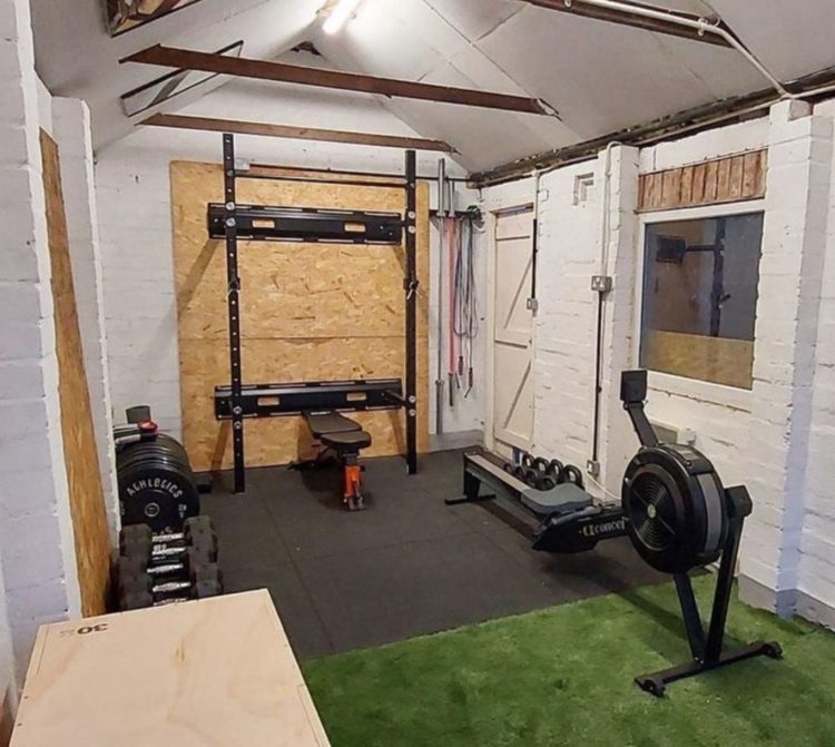 a garden gym with racks fixed to the wall, free weights and exercise machinery