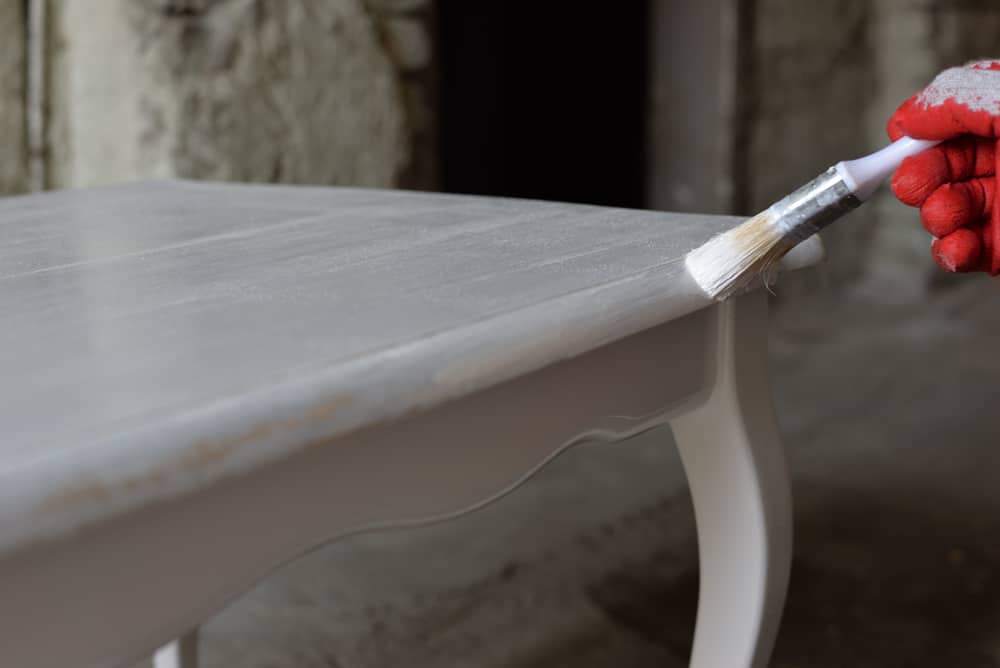 How to Paint Garden Furniture 6 paintbrush in hand and painting on the wooden table