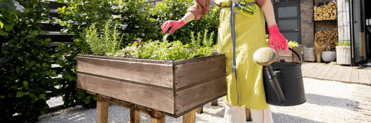 7 Best Waterproof Liners For Planter Boxes (How to Use) 1 A woman tending to flowers in her lined wooden planter box